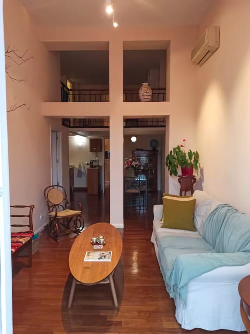 Spacious Madrid apartment living room with wooden floors, blue sofa, round table, rocking chair, potted plants, and two doors