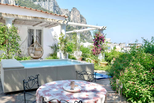 Terrazza di lusso a Capri con vasca idromassaggio, zona pranzo e suggestivo sfondo di scogliere sotto il sole mediterraneo