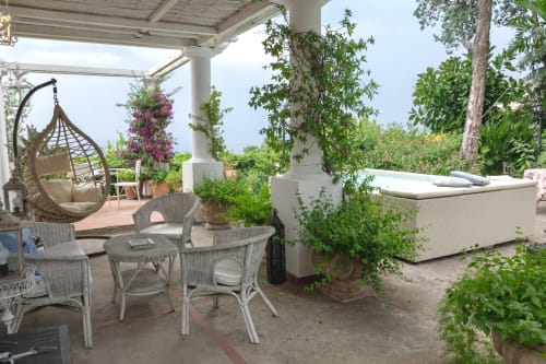 Lussuosa terrazza di villa a Capri con mobili in vimini, sedia sospesa, rampicanti fioriti e vista sul mare