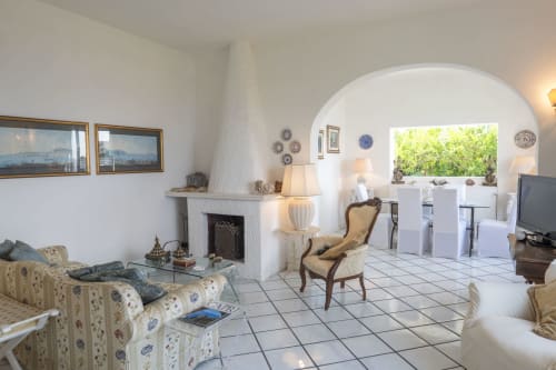 Ampio soggiorno di villa a Capri con camino, arredi eleganti e vista mare dalla finestra ad arco