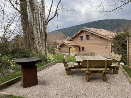 Jardin de chalet en bois avec table de pique-nique, brasero et montagnes boisées à Gérardmer
