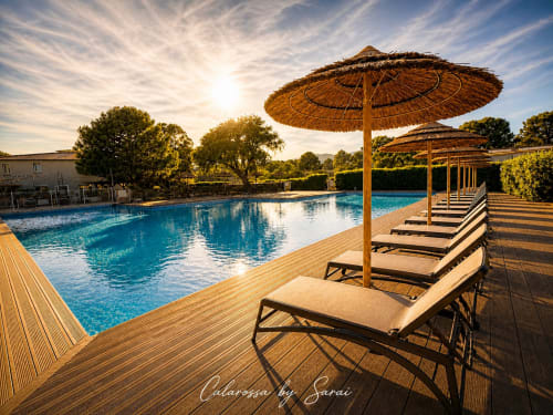 Calarossa Pool bei Sarai mit Liegestühlen und Sonnenschirmen mit Blick auf die Landschaft von Lecci bei Sonnenuntergang