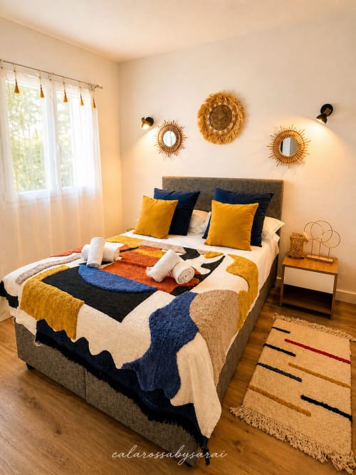 Helles Schlafzimmer im Calarossa By Sarai in Lecci mit farbenfroher Bettwäsche, goldenen Akzenten und modernen Wandspiegeln.