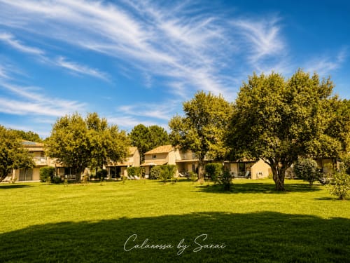 Calarossa, Sarai Luxusanwesen in Lecci mit gepflegten Rasenflächen, Steingebäuden und alten Bäumen unter blauem Himmel