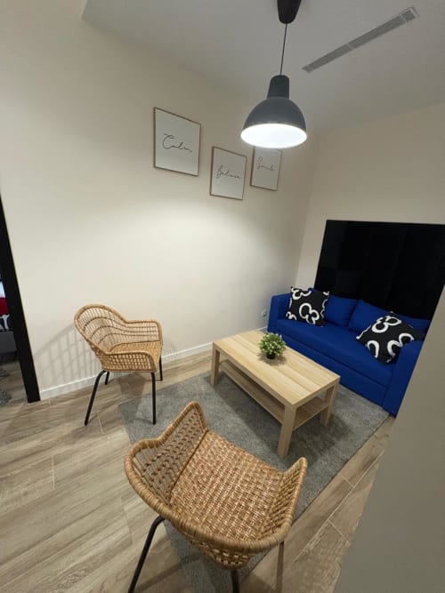 Sala de estar moderna en apartamento de Valencia con sofá azul, sillas de mimbre, mesa de madera e iluminación colgante