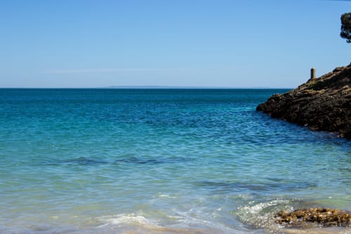 Águas turquesas cristalinas e praia arenosa da Casa Redonda Aroeira, Portugal, com falésias rochosas e mar Mediterrâneo calmo