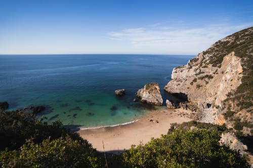 Enseada de praia isolada com águas turquesas e falésias de calcário perto de Casa Redonda Aroeira, Portugal