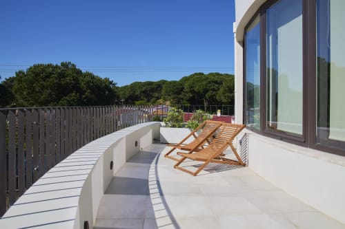Varanda moderna da Casa Redonda Aroeira com espreguiçadeiras de madeira, grades brancas e vistas para pinheiros em Aroeira, Portugal