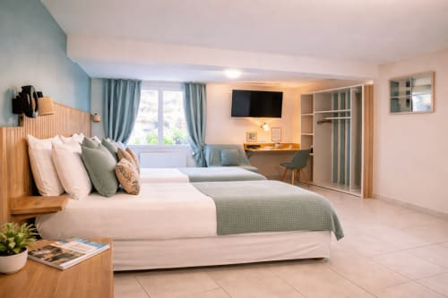 Chambre familiale spacieuse à l'Hôtel De Lion Sur Mer avec deux lits, télévision écran plat, espace de travail et équipements modernes à Lion sur Mer,