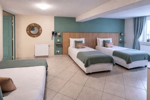 Chambre familiale spacieuse à l'Hôtel De Lion Sur Mer avec trois lits, mur d'accent vert moderne et mobilier confortable