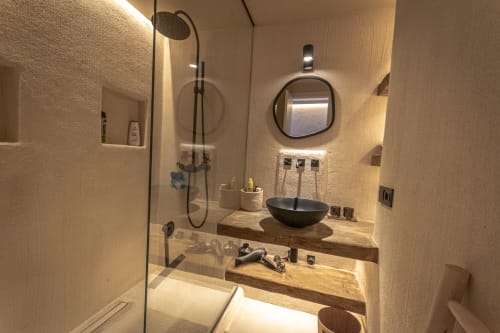 Modern bathroom at Escanda Building Solutions hotel with black vessel sink, wooden countertop, round mirror, and glass shower