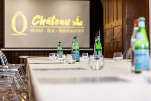 Salle de réunion de l'hôtel Ô Château à Hayange avec table blanche, verres, bouteilles d'eau et écran personnalisé