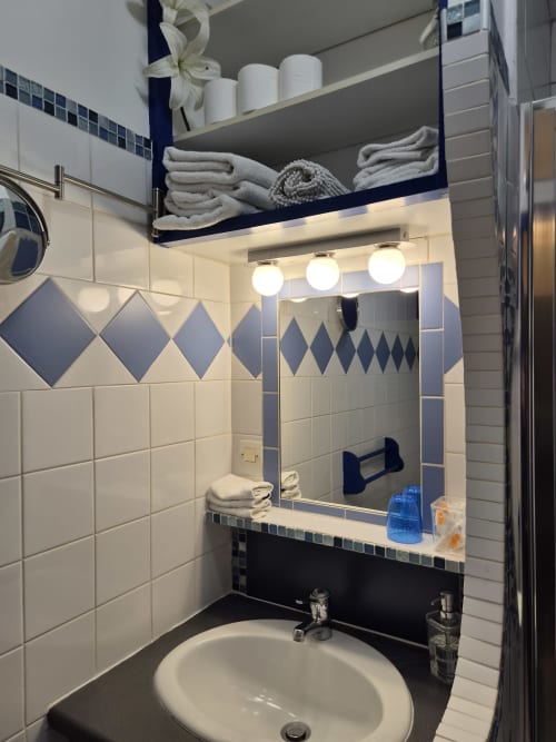 Salle de bains moderne aux carreaux blanc et bleu marine, miroir rétroéclairé, lavabo et étagères de rangement avec serviettes à l'hôtel Orval Et Sens,