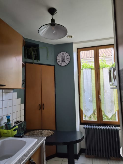 Kitchenette du studio Orval Et Sens avec suspension moderne, meubles en bois, horloge murale et portes sur jardin
