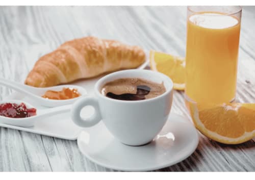 Petit-déjeuner continental à l'hôtel Ô Château avec croissant, café, jus d'orange et agrumes