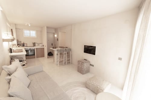 Modern studio apartment at Escanda Building Solutions hotel in Spain with beige décor, kitchen, TV, and comfortable seating.