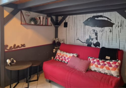Studio cosy Orval Et Sens à Orvault avec canapé rouge, coussins géométriques, bureau en bois et parapluie Banksy