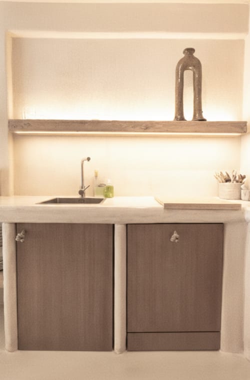 Minimalist kitchenette with cream walls, wooden shelves, metal sink, dark cabinetry, and decorative items at Escanda Building