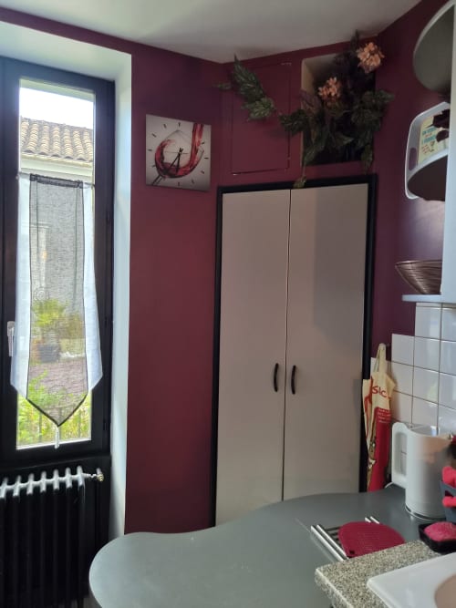 Kitchenette d'Orval Et Sens aux murs bordeaux, mobilier beige, horloge, plantes en pot et vue sur fenêtre à Orvault