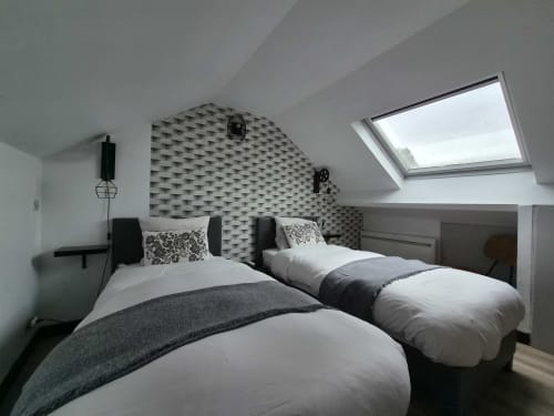 Lits jumeaux avec literie grise et blanche dans une chambre mansardée moderne de l'hôtel Orval Et Sens à Orvault, avec lucarne et motifs