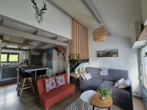 Séjour spacieux en open-plan avec canapé rouge, fauteuil gris, table en bois et cuisine à l'appartement Orval Et Sens à Orvault