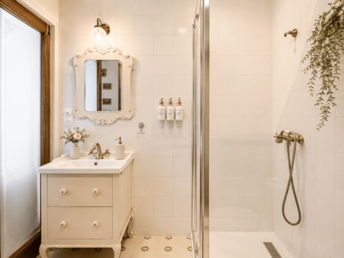 Elegante baño en la Casa Celso de Baiona, con tocador color crema, espejo ornamental, ducha de lluvia y detalles verdes