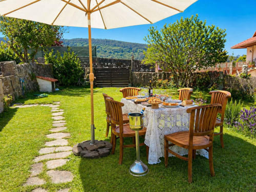 Comedor al aire libre en la casita Casa Celso de Baiona con sillas de madera, sombrilla y vistas a la montaña