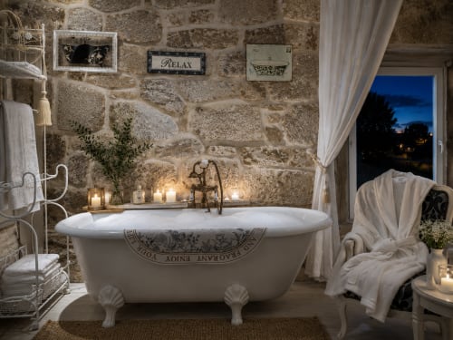 Baño lujoso con bañera independiente, muros de piedra, luz de velas y vistas al jardín en Casa Celso