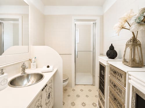 Baño elegante en la casa rural Casa Celso cerca de Baiona con paredes de azulejos blancos, lavabo de cerámica, inodoro, ducha y detalles decorativos