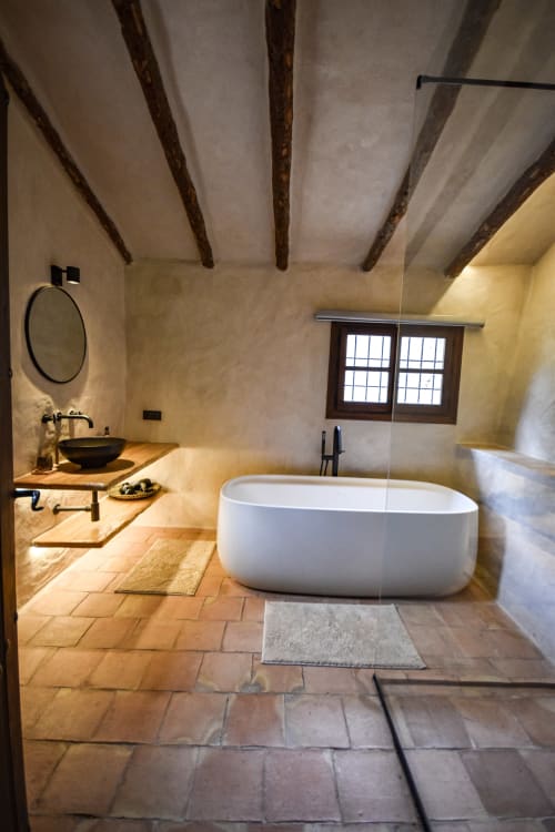 Luxury bathroom at Escanda Building Solutions hotel with freestanding white bathtub, terracotta flooring, wooden beams, and