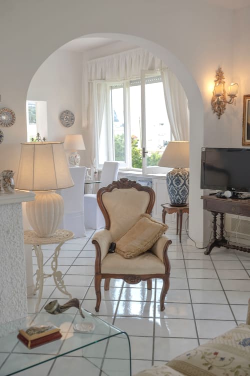 Elegante soggiorno di La Capperina a Capri, con portale ad arco, poltrona color crema e vista sul mare
