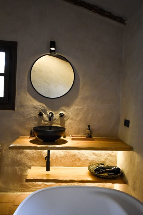 Modern minimalist bathroom with black vessel sink, round mirror, wooden countertop, and textured stone walls at Escanda