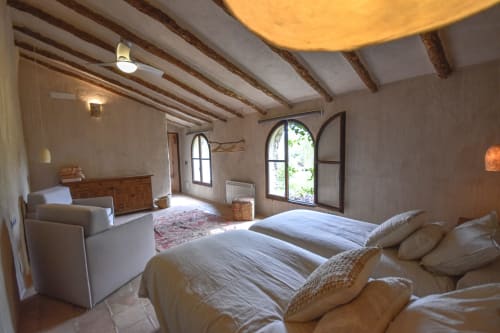 Spacious hotel bedroom with exposed beams, twin beds, lounge area, and arched windows overlooking gardens at Escanda Building