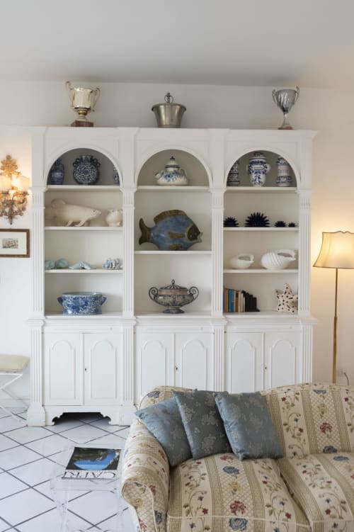 Elegante vetrina bianca con porcellana blu e bianca, pesci decorativi e libri a La Capperina, Capri