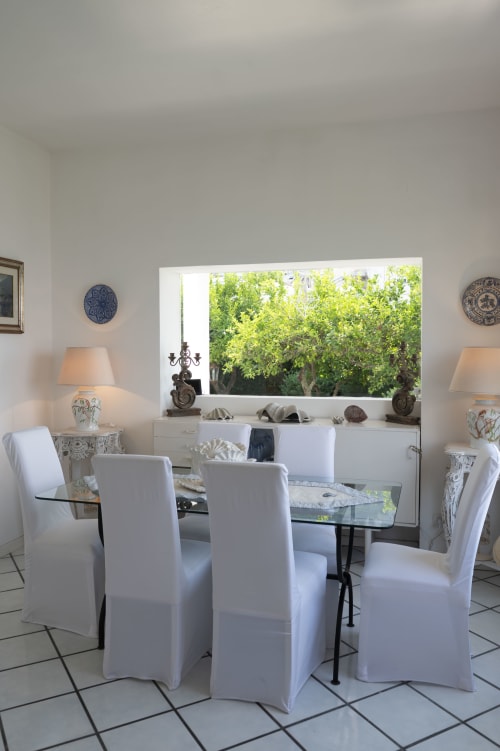 Elegante sala da pranzo de La Capperina a Capri con sedie rivestite bianche, tavolo in vetro e vista sul giardino