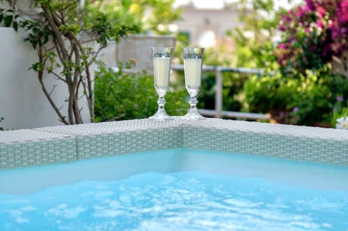 Due flute di champagne accanto alla piscina blu dell'hotel La Capperina a Capri con giardini in fiore