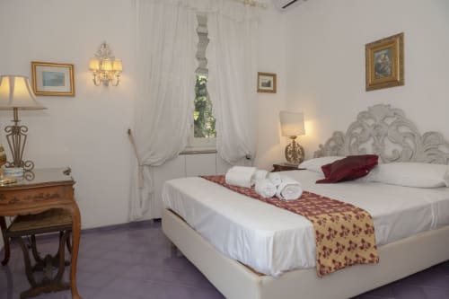 Elegante camera da letto all'hotel La Capperina di Capri con biancheria bianca, testata decorativa e arredi classici