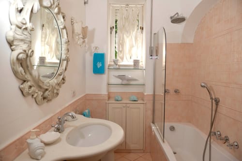 Bagno elegante di La Capperina a Capri con piastrelle color pesca, specchio ornamentale, doccia a pioggia e arredamento costiero