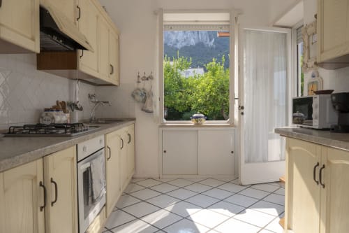 Luminosa cucina color crema a La Capperina a Capri con mobili crema, piani in pietra grigia e vista sul giardino rigoglioso e le montagne