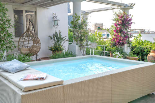 Piscina sul tetto dell'hotel La Capperina a Capri con sdraio, altalena in vimini e buganvillea in fiore.