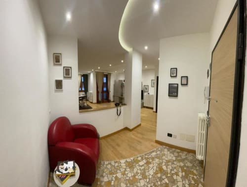 Ingresso MiSaNi Apartments Novara con sedia rossa moderna, pavimentazione in legno e design contemporaneo del soffitto