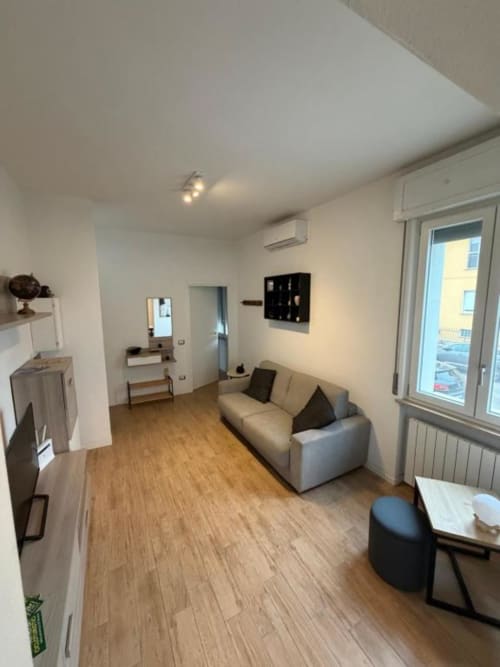 Moderno soggiorno dell'appartamento MiSaNi Apartments Novara con divano beige, pavimento in legno e porte finestre in vetro