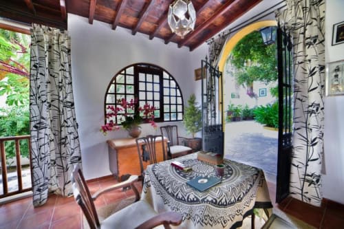 Interior del Cortijo San Ignacio: sala rústica con vigas de madera, ventana arqueada, cortinas estampadas y vista al patio