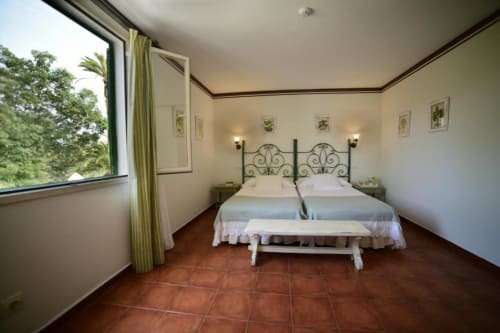 Dormitorio doble en Cortijo San Ignacio con cabecero de hierro forjado, suelos de terracota y vistas al jardín