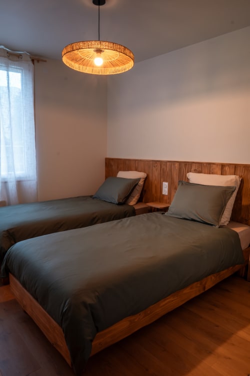 Chambre twin à la Maison Antea B&B au Puy-en-Velay avec lits en bois, literie foncée et luminaire suspendu tressé