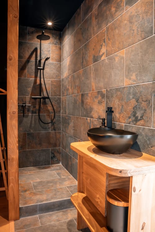 Salle de bains moderne à la Maison Antea avec meuble vasque en bois rustique, lavabo en pierre noire et douche en ardoise avec pomme de douche effet pluie