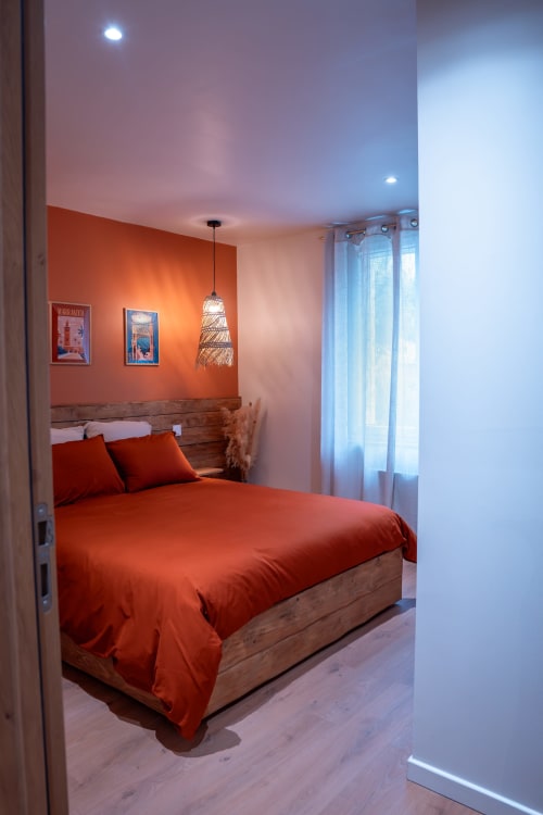 Chambre moderne à la Maison Antea au Puy-en-Velay avec mur d'accent orange, lit en bois et luminaires suspendus