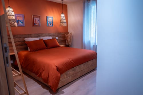 Chambre moderne à la Maison Antea B&B au Puy-en-Velay avec literie orange, tête de lit en bois, luminaires suspendus et tableaux encadrés