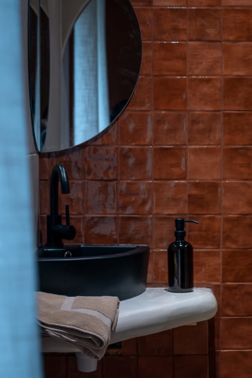 Lavabo noir moderne avec miroir rond à la Maison Antea B&B au Puy-en-Velay, fond de carrelage en terre cuite