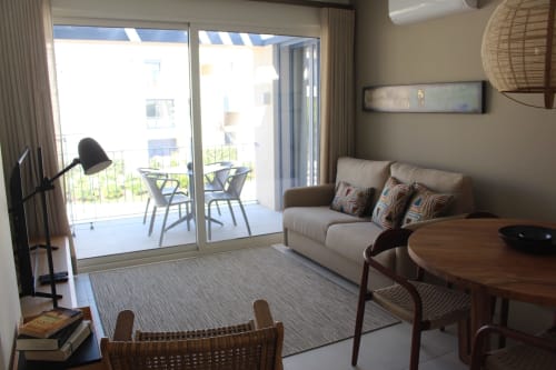 Quarto moderno do Break Lovers com sofá bege, móveis de madeira e portas de vidro corrediço abrindo para varanda com vista da cidade
